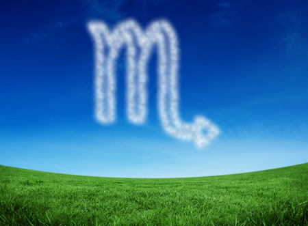 Cloud in shape of scorpio star sign against green field under blue skyの写真素材