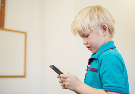 Cute pupil using smartphone in classroom at the elementary school