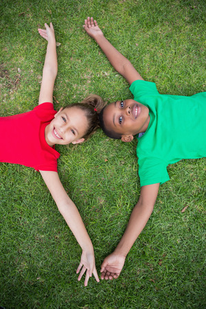 Cute children smiling at camera outside on the grass in the parkの写真素材