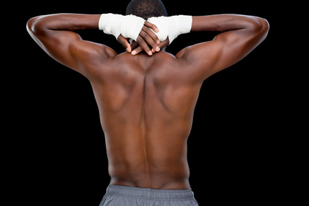 Rear view of a shirtless muscular man standing over black background