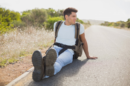 Full length of a hiking man sitting on countryside roadの写真素材