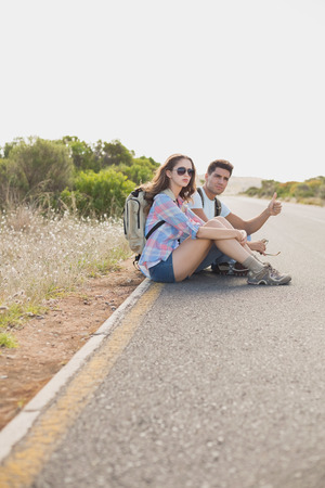 Full length of young couple hitchhiking on countryside roadの写真素材
