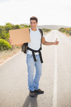 Portrait of a cheerful man hitchhiking with cardboard on countryside roadの写真素材