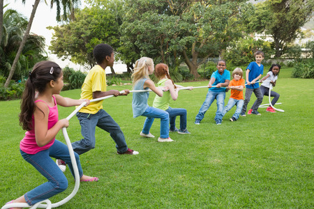 Cute pupils playing tug of war on the grass outside  at the elementary school