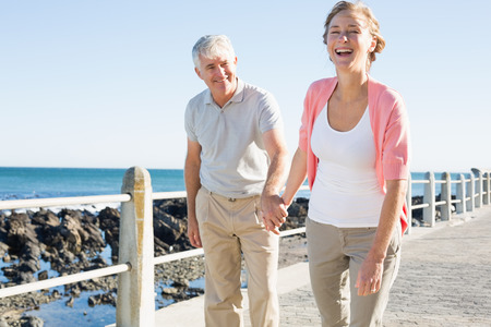 Happy casual couple walking by the coast on a sunny dayの写真素材