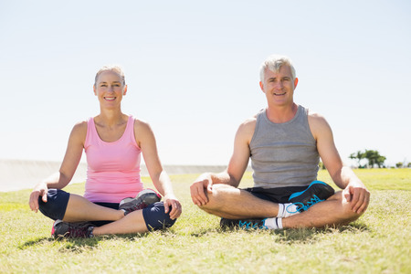 Fit mature couple sitting in lotus pose on the grass on a sunny dayの写真素材