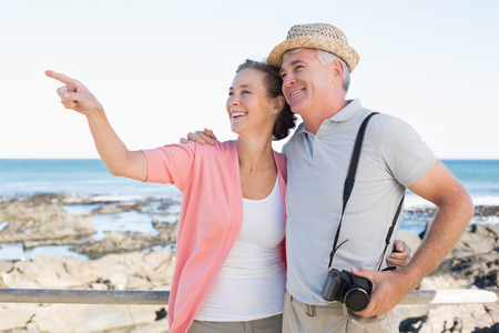 Happy casual couple looking at something by the coast on a sunny dayの写真素材