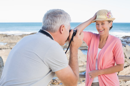 Happy casual man taking a photo of partner by the sea on a sunny dayの写真素材