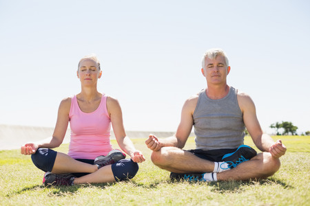Fit mature couple sitting in lotus pose on the grass on a sunny dayの写真素材