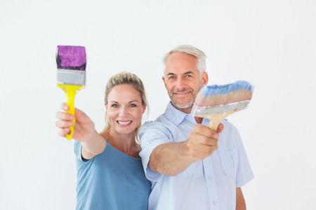 Happy couple holding paintbrushes smiling at camera on white backgroundの写真素材
