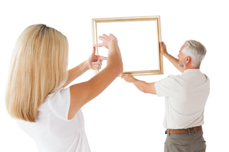 Couple hanging a frame together on white backgroundの写真素材