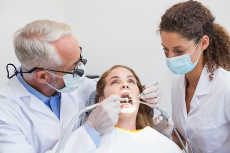 Dentist examining a patients teeth in the dentists chair with assistant at the dental clinicの写真素材