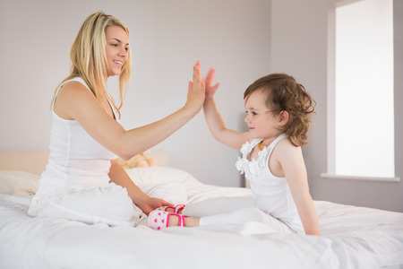 Side view of mother and daughter high fiving on bed at homeの写真素材
