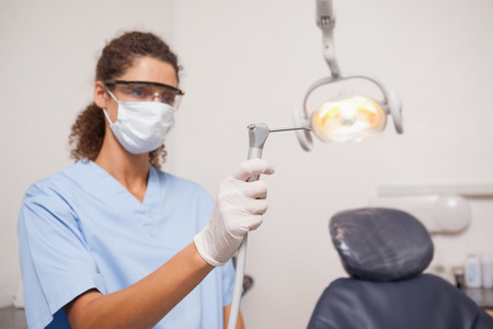 Dentist in mask and protective glasses holding drill at the dental clinicの写真素材