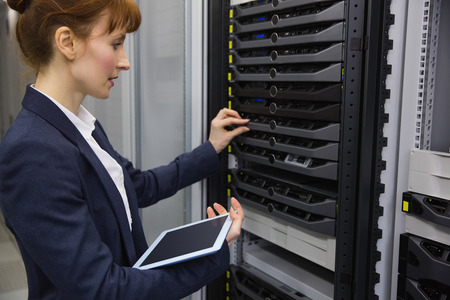 Pretty technician using tablet pc while working on servers in large data center