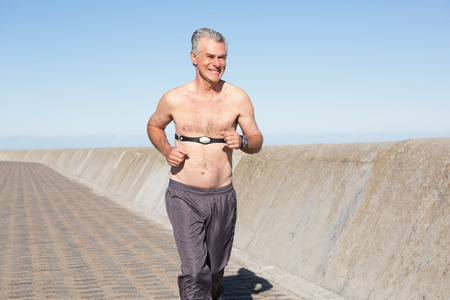Active shirtless senior man jogging on the pier on a sunny dayの写真素材