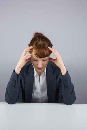 Stressed businesswoman sitting at desk on grey backgroundの写真素材
