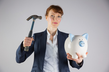 Businesswoman holding hammer and piggy bank on grey backgroundの写真素材