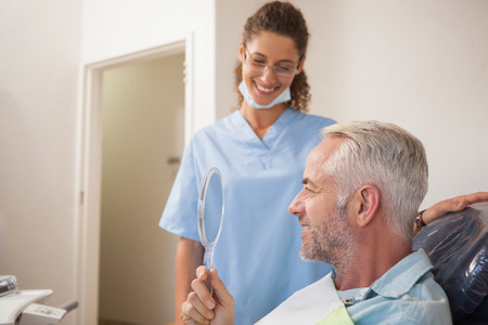 Dentist showing patient his new smile in the mirror at the dental clinicの写真素材