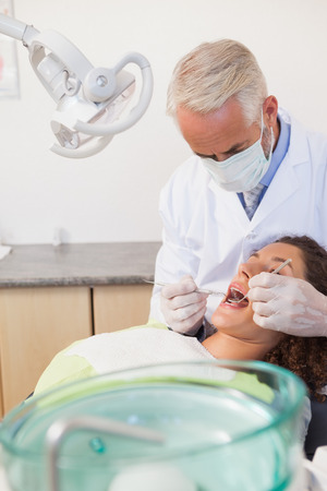Dentist examining a patients teeth in the dentists chair at the dental clinicの写真素材