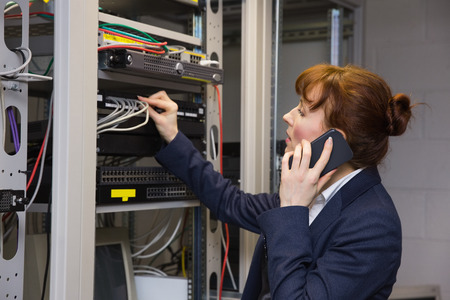 Pretty computer technician talking on phone while fixing server in large data center