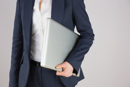 Businesswoman in suit holding laptop on grey backgroundの写真素材