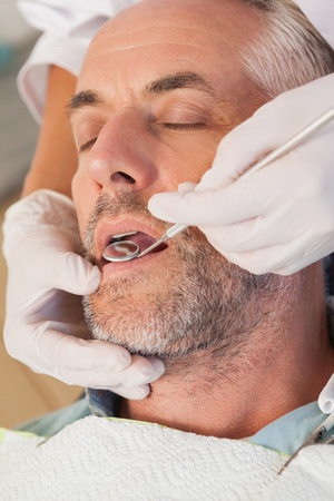 Dentist examining a patients teeth in the dentists chair at the dental clinicの写真素材