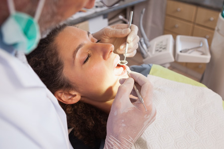 Dentist examining a patients teeth in the dentists chair at the dental clinicの写真素材
