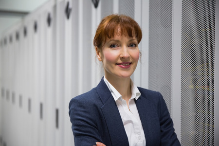 Pretty computer technician looking at camera in large data centerの写真素材