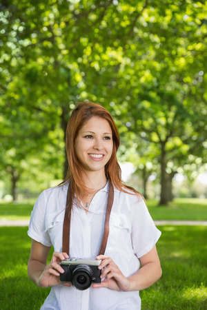 Pretty redhead holding her camera in the park on a sunny dayの写真素材