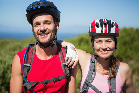 Active couple cycling in the countryside smiling at camera on a sunny dayの写真素材