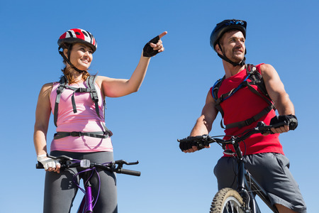 Fit cyclist couple standing at the summit on a sunny dayの写真素材
