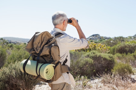 Hiker looking through binoculars on country trail on a sunny dayの写真素材