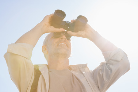 Happy hiker looking through binoculars on a sunny day