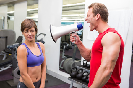 Personal trainer shouting at client through megaphone at the gymの写真素材