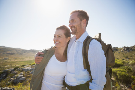 Hiking couple embracing and smiling on country terrain on a sunny dayの写真素材