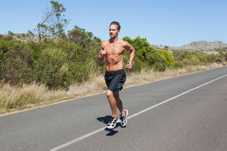 Shirtless man jogging on open road  on a sunny dayの写真素材