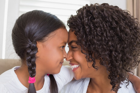 Pretty mother sitting on the couch with her daughter hugging at home in the living roomの写真素材