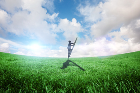 Businessman climbing up ladder against green field under blue skyの写真素材