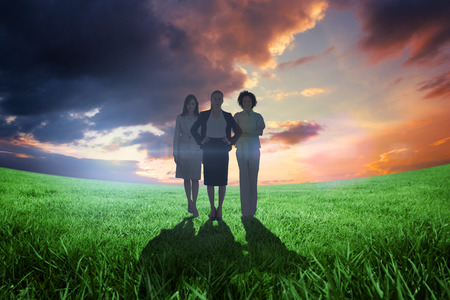 Team of businesswomen looking at camera against green field under orange skyの写真素材