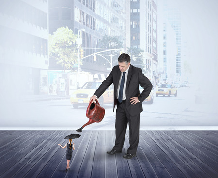 Mature businessman watering tiny businesswoman against urban projection on wallの写真素材