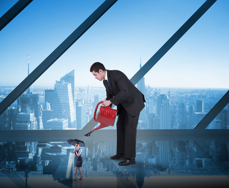 Businessman watering tiny businesswoman against room with large window looking on cityの写真素材