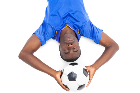 Football player lying on the ground holding ball with eyes closed on white backgroundの写真素材