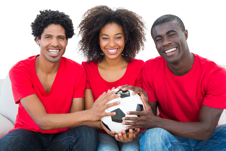 Happy football fans in red holding ball together on white backgroundの写真素材