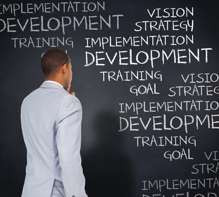 Thinking businessman against blackboard with business buzzwordsの写真素材