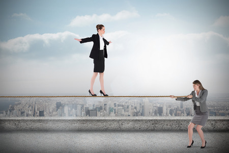 Young businesswoman pulling a tightrope for business woman against balcony overlooking cityの写真素材