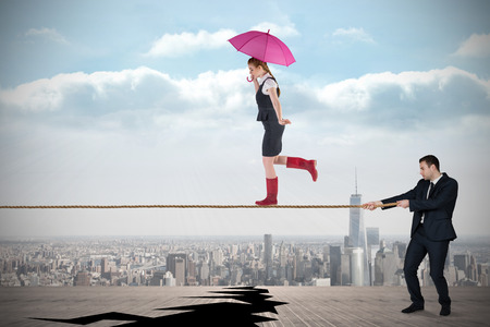 Young business man pulling a tightrope for businesswoman against cracked balcony overlooking cityの写真素材