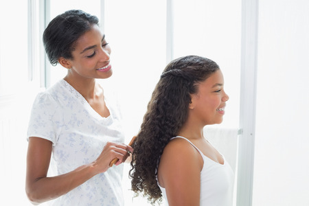 Pretty mother brushing her daughters hair at home in bathroomの写真素材