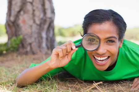 Pretty environmental activist looking at camera through magnifying glass on a sunny day in the countrysideの写真素材
