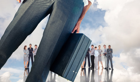 Businessman holding briefcase against blue sky with white clouds and business peopleの写真素材